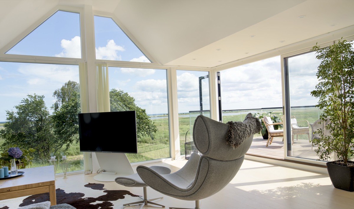 Stue med hjørnekvist i glas, panoramaudsigt over eng og udgang til terrasse