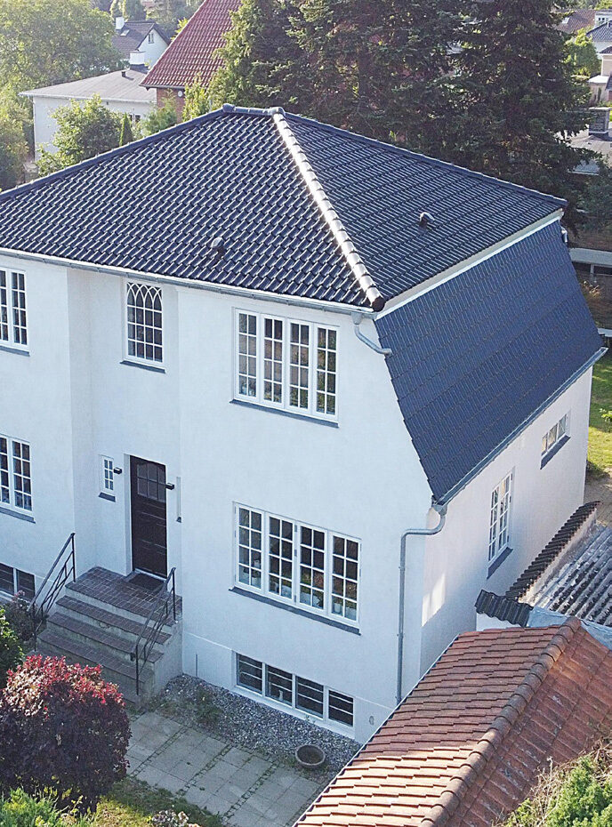 Hvidpudset villa i to etager med sort tegltag, set skråt ovenfra