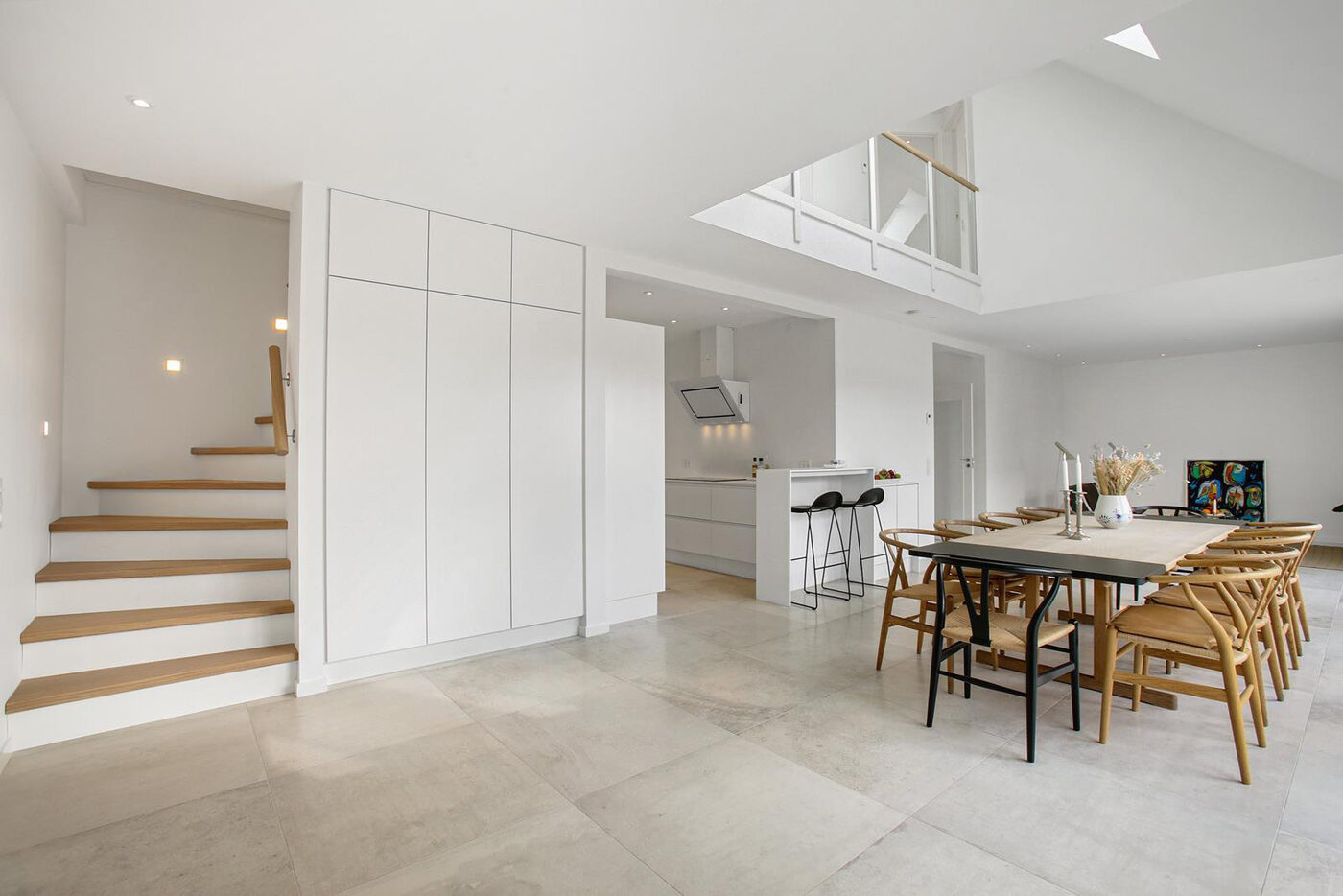 Lyst spisekøkken med dobbelthøjt loft, trappe til førstesal og ovenlys