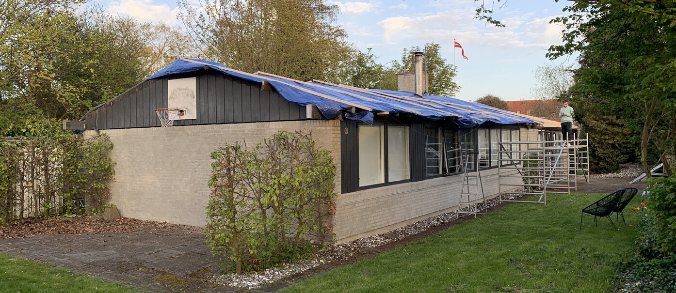 Huset set fra haven med blå presenninger over hele tagfladen under arbejdet